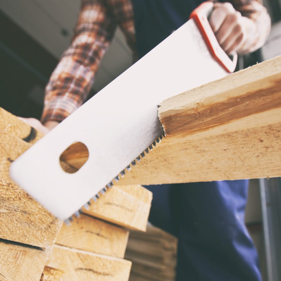 The carpenter is cutting the wooden plank by the saw